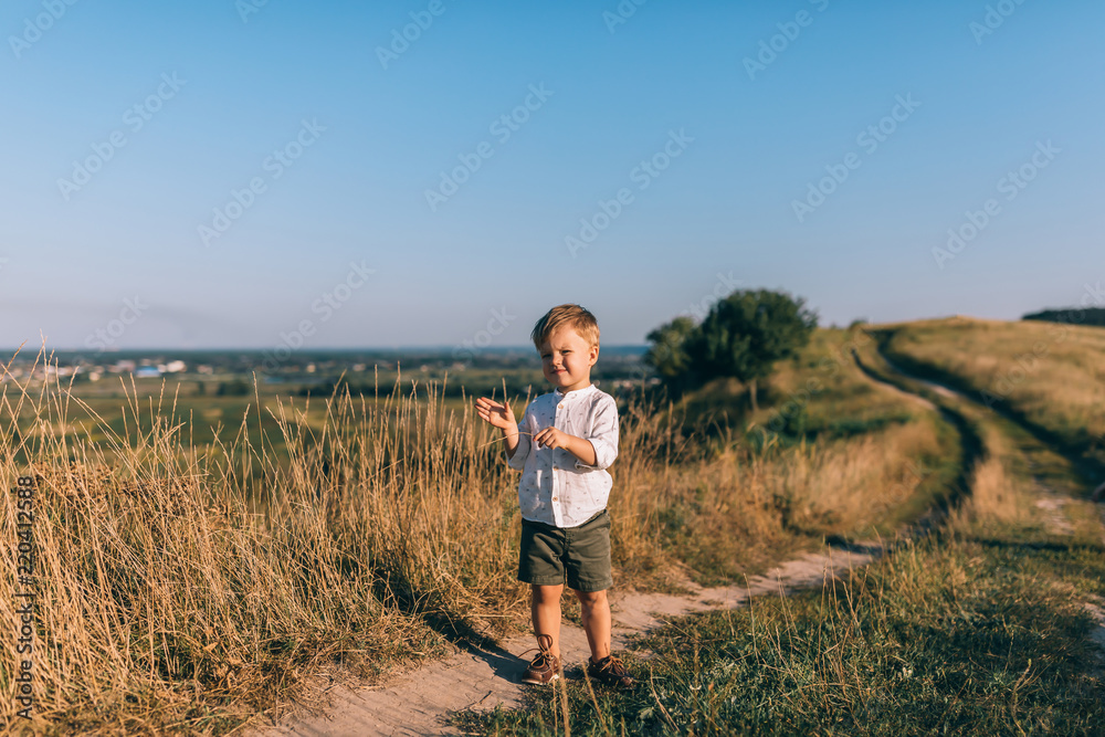 full length view of cute little boy standing on rural path and looking at camera