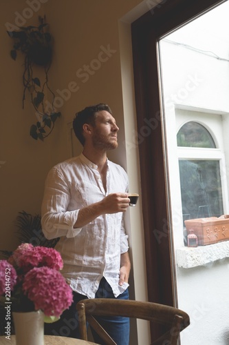 Man having coffee while standing near window at home