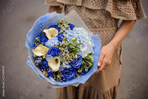 Girl in beige dress holding a romantic bouquet of flowers in blue tones