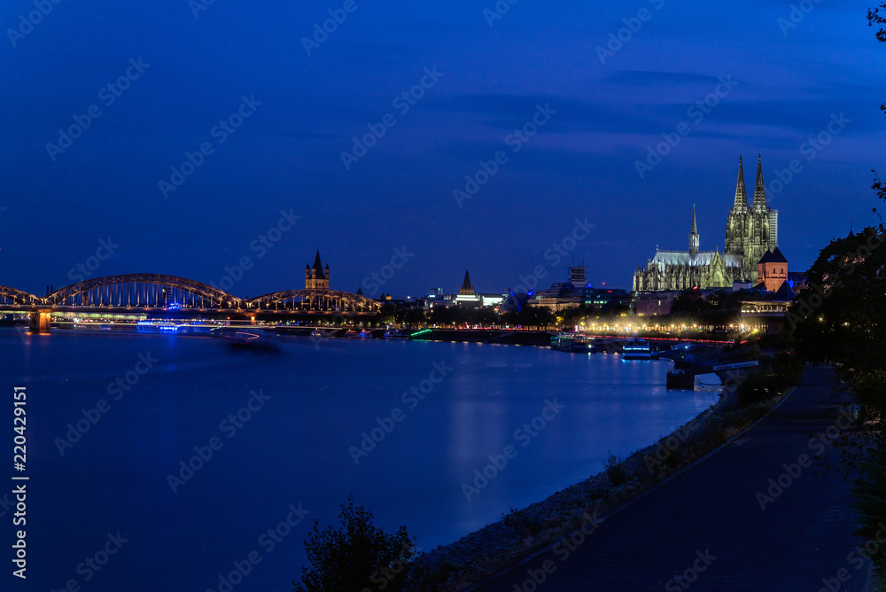 Naklejka premium Dome of the City of Cologne, Gemany on the right, Rhine River on the left at blue hour