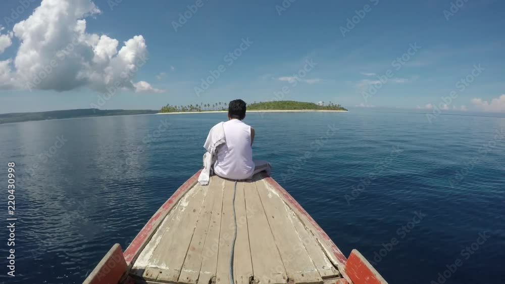 Happy man sitting on the front of small boat going to tropical paradise island