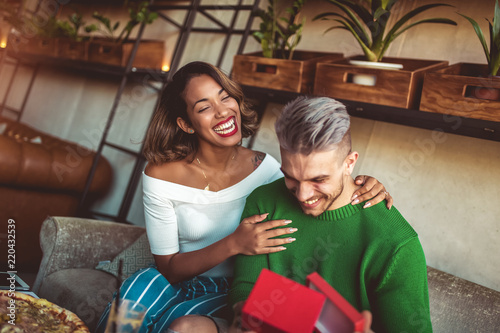 Happy  interracial couple sitting in cafe bar. Man giving gift to his girlfriend. photo