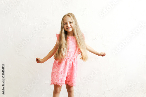 Little blonde girl with long golden hair dancing, smling and having fun over white textured plaster wall background. Five years old blonde female child posing. Copy space for text.