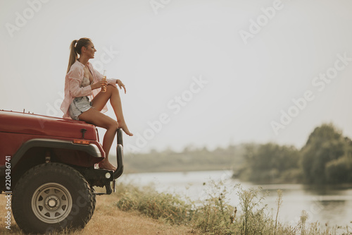 Young woman sits on a car hood and drinks refreshment photo