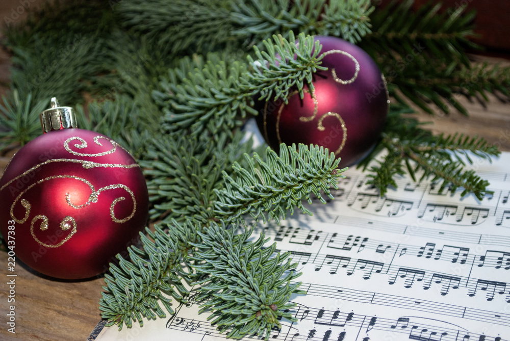 Fototapeta premium Alte Musiknoten mit roten Weihnachtskugeln und Tannenzweig, Weihnachten, xmas