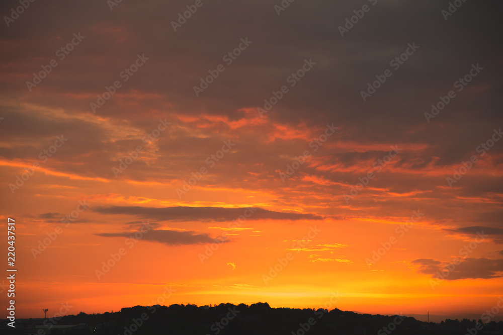 Evening sky after sunset with red clouds and the silhouette of the private sector of a small town