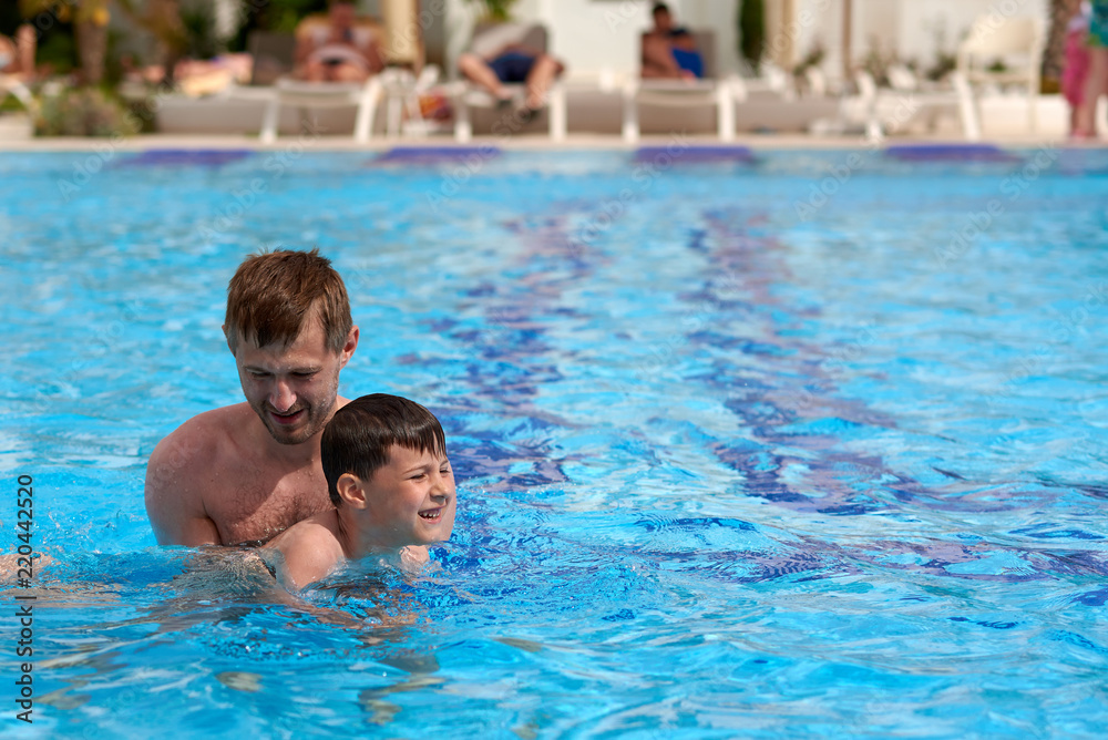Father and son learning to swim in the swimming pool at the hotel.