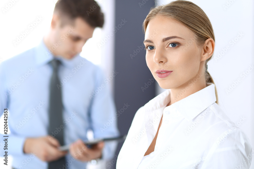Beautiful blonde businesswoman standing straight in a brightly lit office at the background of colleagues or partners. Business concept