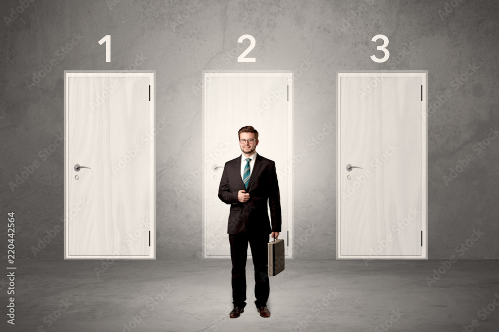 Fototapeta premium Businessman in grey room with three numbered white door behind his back 