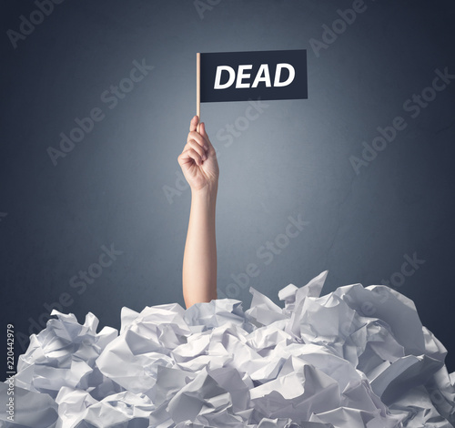 Female hand emerging from crumpled paper pile holding a black flag with dead written on it