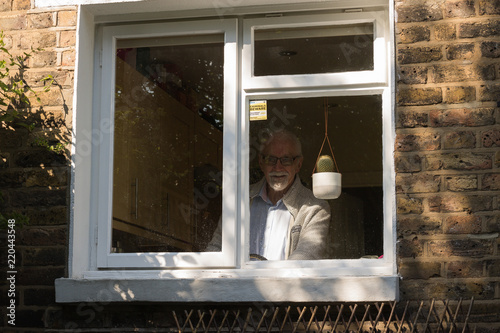 An elderly man looks out through a window and smiles. On the window there is a pretty plant cactus and an inscription "criminals beware".