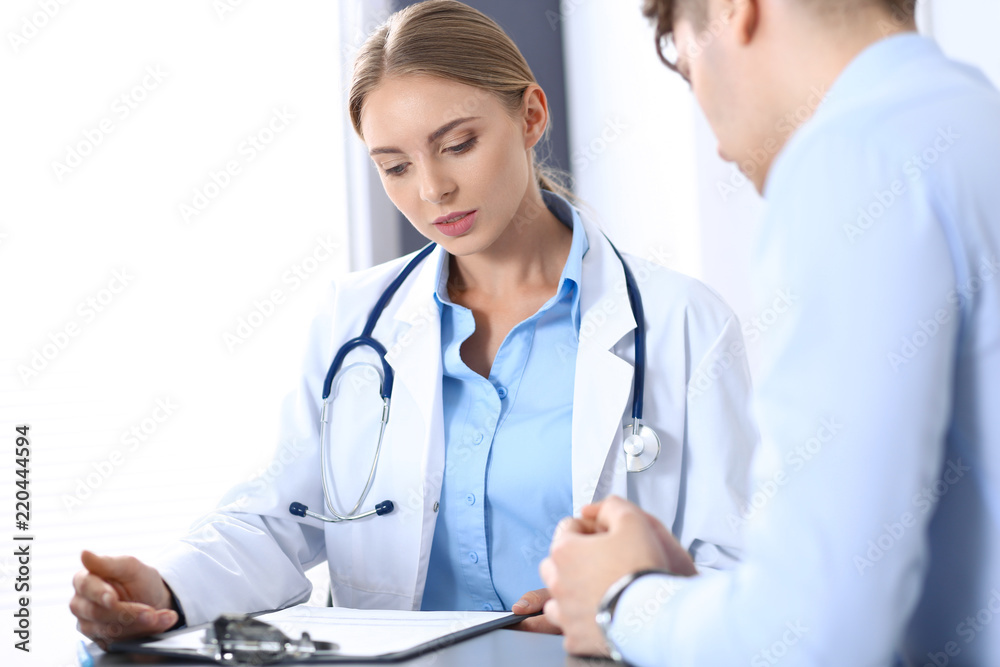 Doctor and patient in hospital. Beautiful blonde physician consulting business man about his health. Medicine concept Doctor and patient in hospital. Beautiful blonde physician consulting business man about his health. Medicine concept