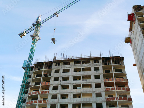 Industrial crane and building against blue sky. Concrete building under construction. Construction site background.