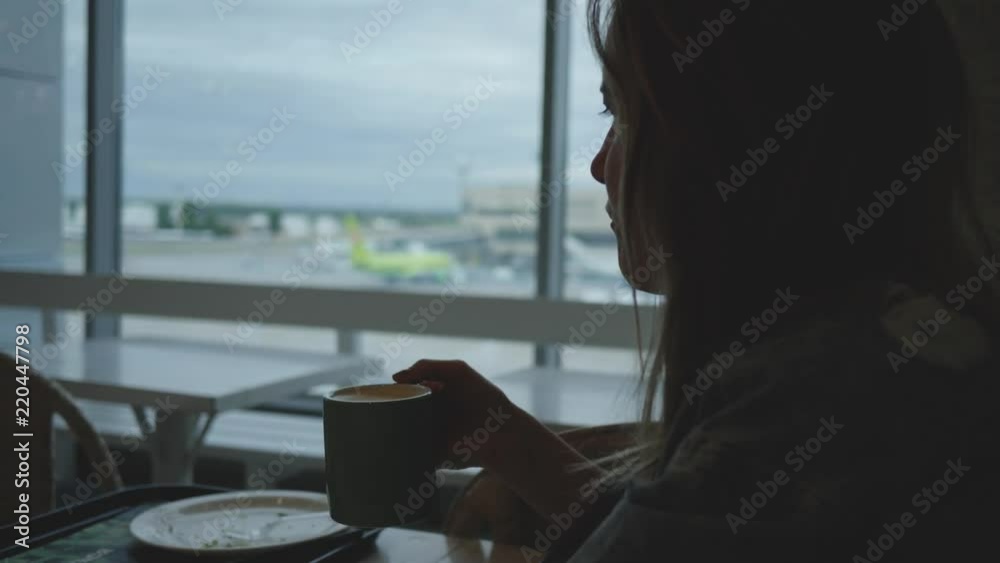 Young woman drinks coffee in airport caffee waiting for departure