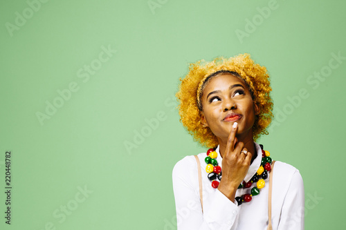 Young woman thinking and looking up, isolated on green studio background