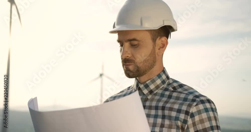 Close up of the handsome wind renewable power station worker in the halmet checking some document and drawing. photo