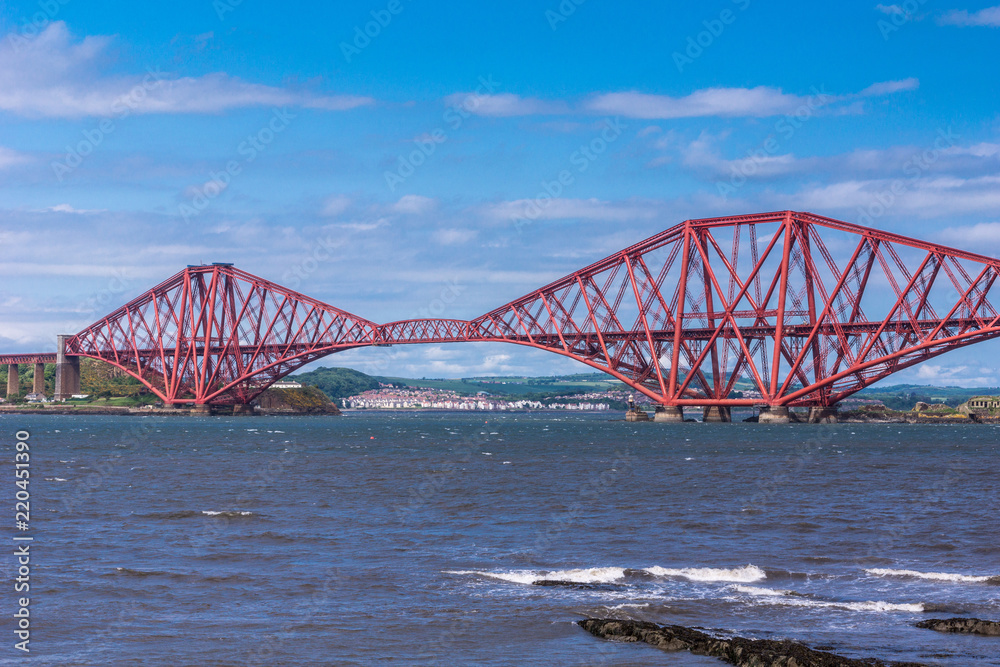 Queensferry, Scotland, UK - June 14, 2012: Closeup of Red metal iconic Forth Bridge for trains over Firth of Forth between blue sky and blue water.