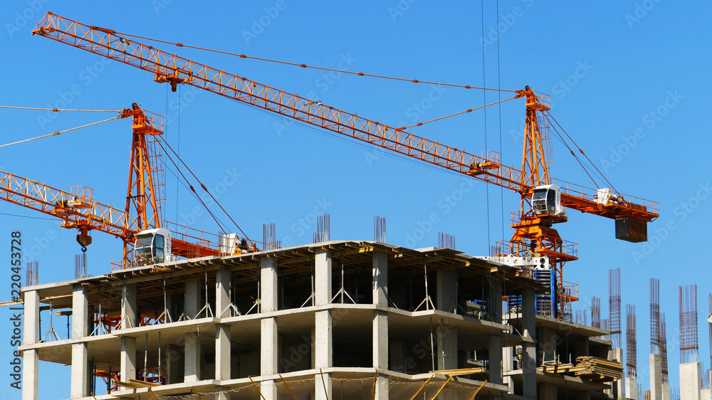 Two construction cranes and concrete building under construction