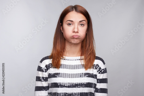 Offended upset young stylish female blowing cheeks, has grumpy expression, poses against white background, being unsatisfied and disappointed after conflict with teacher or colleagues, makes grimace.