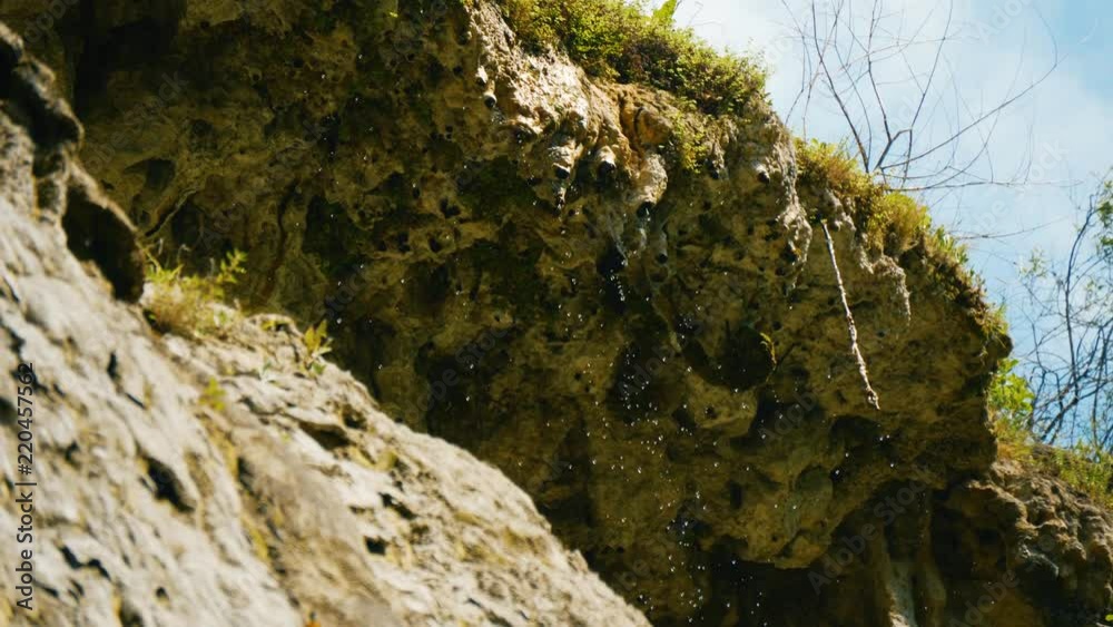 Water flows and drops from steep rock slope. Low angle view on overhang Water flows and drops from steep rock slope. Low angle view on overhang