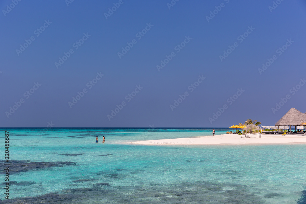 Maldives, Feb 8th 2018 - Tourists swimming in a turquoise blue sea, desert island, small traditional hut hotel on a blue sky day, paradise feeling in Maldives.