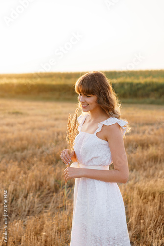 Girl in white dress with spikelets. Woman in field, place for text. Spike and girl in field. Late summer and early autumn. August or September
