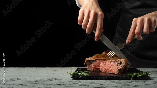 Quadro su tela Chef, cut with a meat steak on a black background with an open space for text or restaurant menus