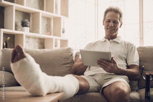 Man With Fractured Leg Sit On Sofa and Use Tablet