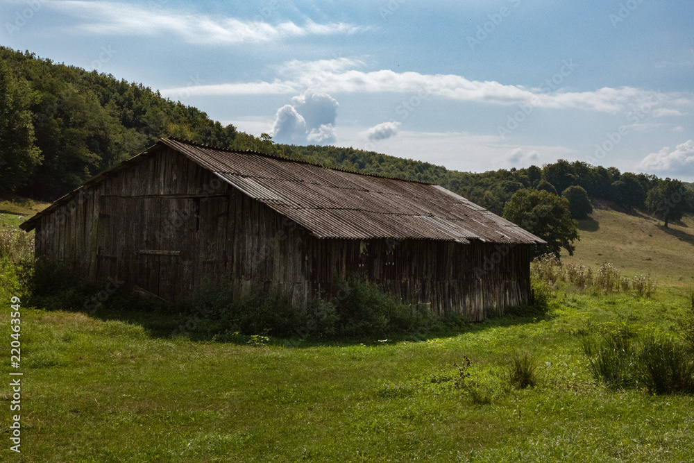 A barn on a green meadow with haystacks on a sunny day with blue sky and white clouds. A barn on a green meadow with haystacks on a sunny day with blue sky and white clouds.