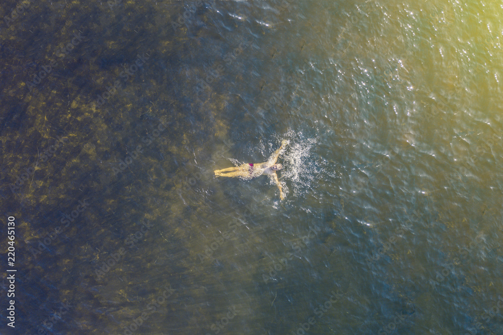 Fototapeta premium top high aerial view of lonely person swim in the sea in a summer heaven lagoon beach