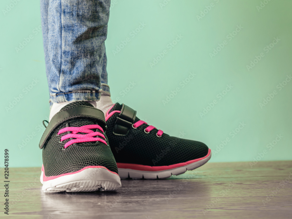 The girl's legs in torn jeans and black and red sneakers on the brown wooden floor near the blue wall. The girl's legs in torn jeans and black and red sneakers on the brown wooden floor near the blue wall.