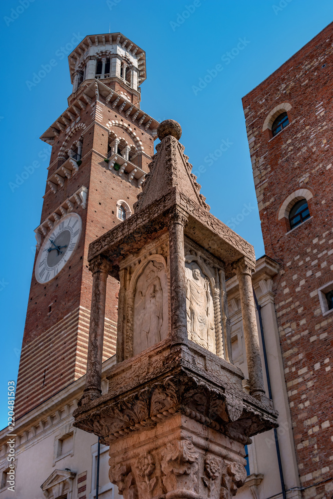 Ancient column on Erbe square in Verona. On the column there is the coat of arms of the Visconti family and a relief image of the figures of the saints. In the background is the Lamberti tower
