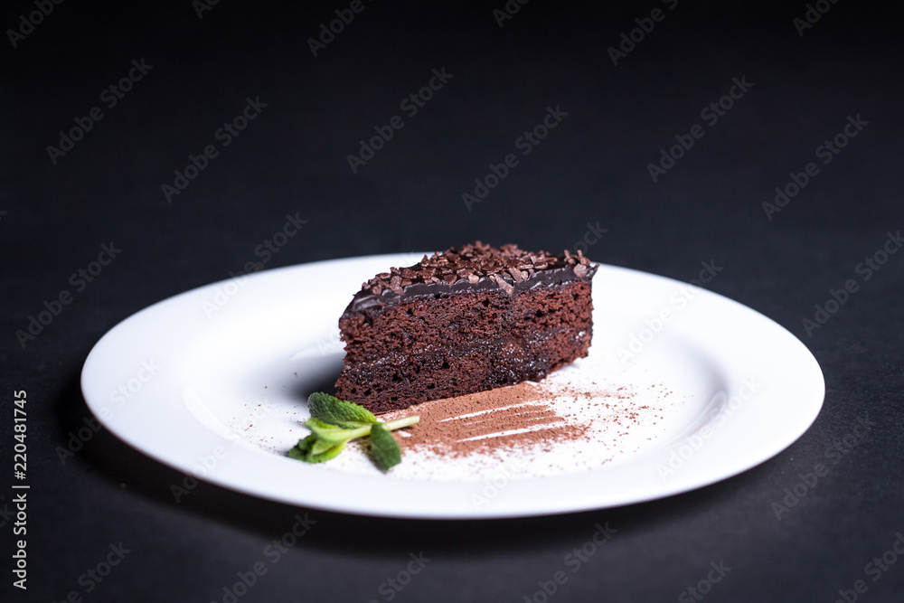 Delicious chocolate cake on a white plate. Isolated on a dark background. Delicious chocolate cake on a white plate. Isolated on a dark background.