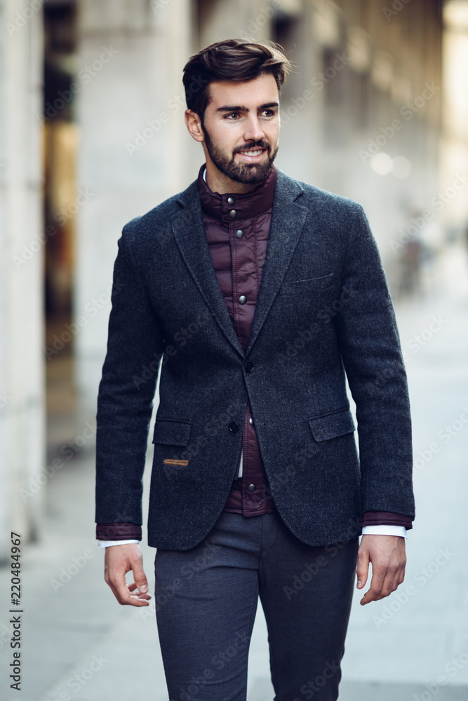Young bearded man smiling in urban background wearing british elegant suit in the street. Young bearded man smiling in urban background wearing british elegant suit in the street.