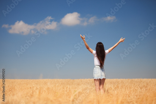 Happy woman enjoying the life in the field Nature beauty, blue cloudy sky and colorful field with golden wheat. Outdoor lifestyle. Freedom concept. Woman in summer field