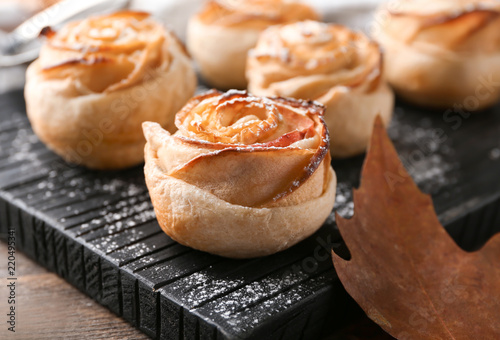 Wooden board with apple roses from puff pastry on table, closeup