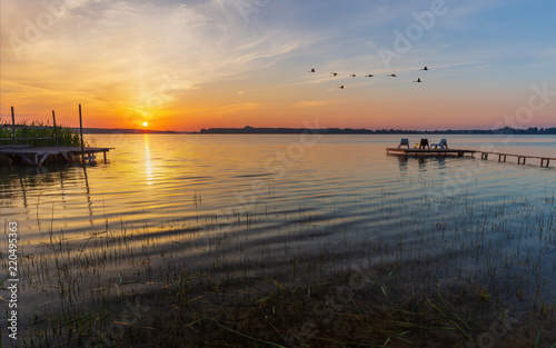 Obraz na płótnie Wooden footbridge and flying swans during sunrise at Powidzkie lake in Poland. w salonie