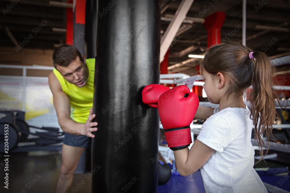 Little girl training with coach and punchbag in boxing gym