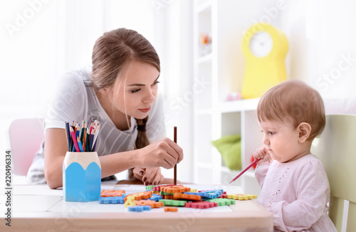 Cute little girl with young nanny at table, indoors