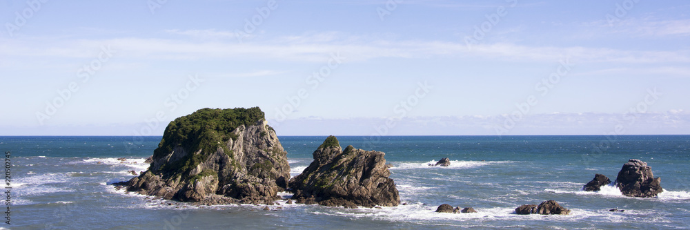 Panorama view on the beautiful New Zealand west coastal area, with the Tasman Sea, rocks, blue water and a clear sky. This is a rough, untamed and sparsely populated region of the South Island