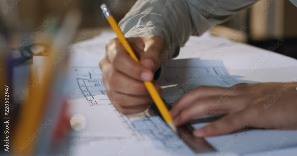 Male Caucasian hands drawing on the plan with a pencil and rule on the table. Close up of the architect working.