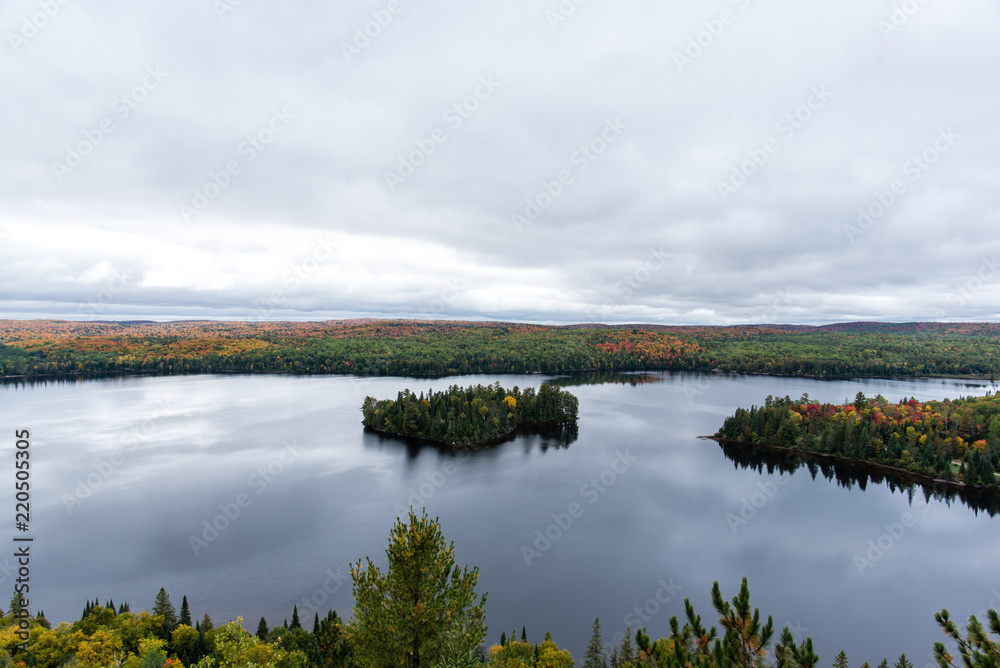 It is a picture of red maple taken in Canada. This is a picture of autumn leaves seen from Algonquin State Park in Ontario, Canada. There are colorful autumn leaves around the lake.