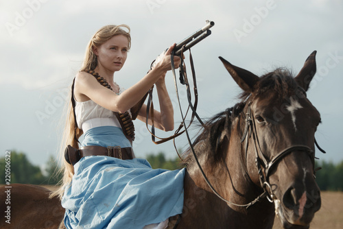 Fényképezés Portrait of a beautiful female cowgirl with shotgun from wild west riding a horse in the outback