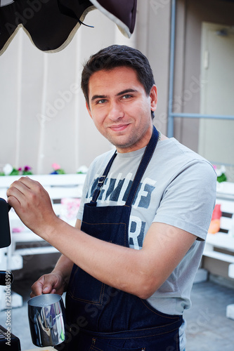 Attractive guy in apron using coffee machine and looking at camera while working in cafe