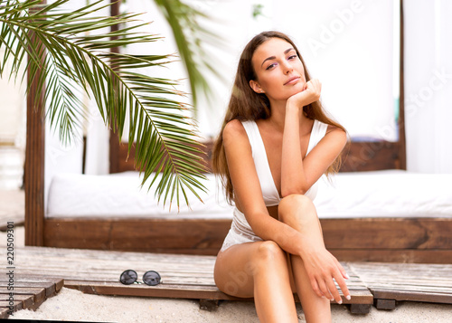 fashion girl in a swimsuit sits on the beach in tropical palms