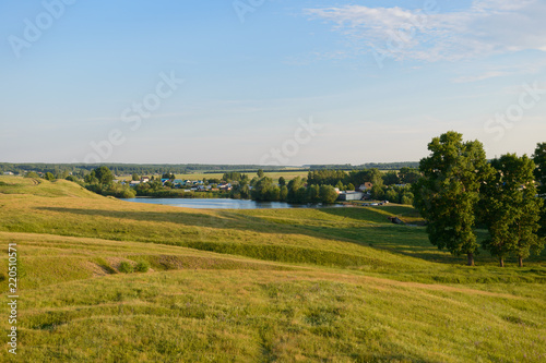 evening summer landscape with a village, a pond, meadows and fields