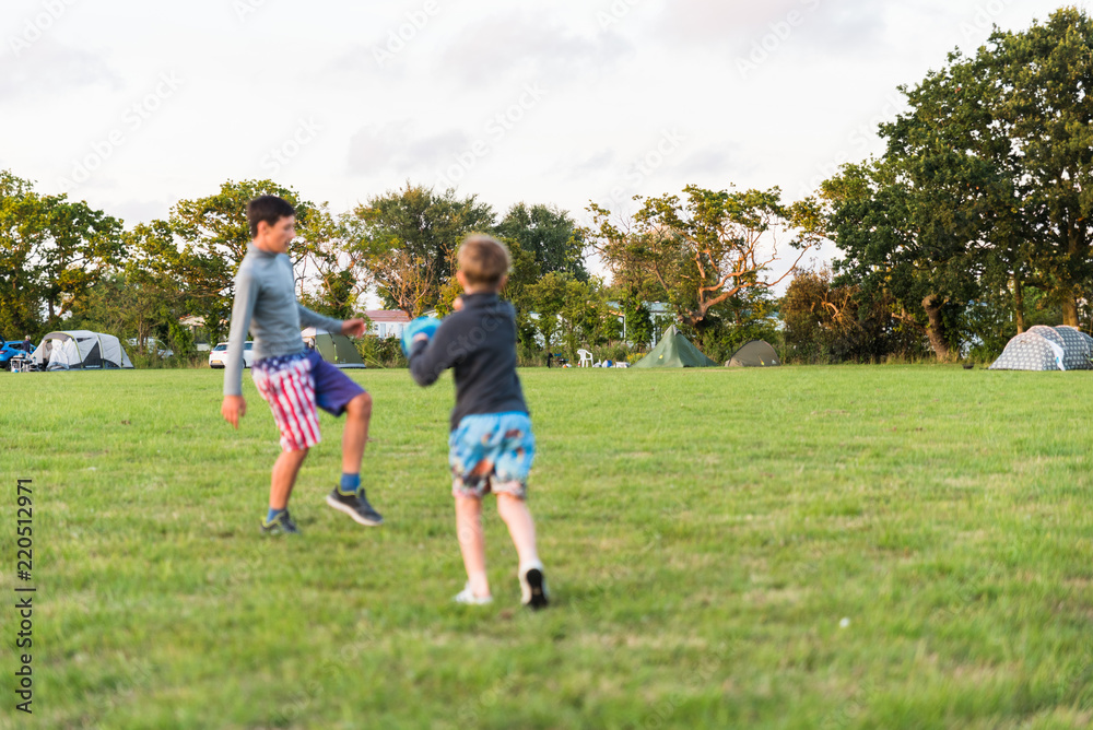 two brother boys not in focus playing with ball and having fun together over camping field in England two brother boys not in focus playing with ball and having fun together over camping field in England