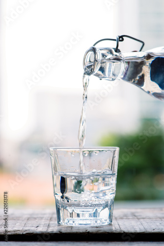 Clean drinking water is poured from a jug into a round glass cup on a wooden table and a light green napkin close-up macro on a green nature outdoors background Fototapeta