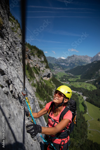 Pretty, female climber on a via ferrata - climbing on a rock in Swiss Alps