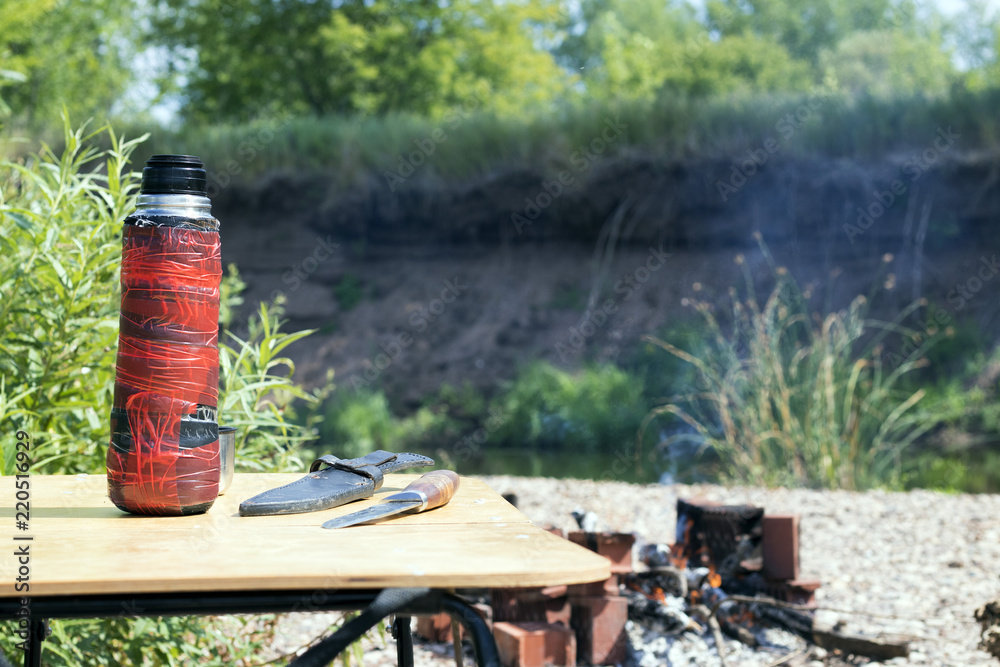 Nature and wooden table on which there is an old thermos, hunting knife, in the summer Nature and wooden table on which there is an old thermos, hunting knife, in the summer